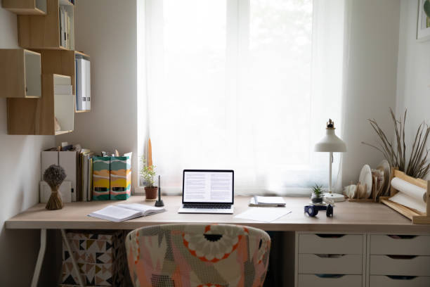 Empty desk workplace in cozy home bedroom with open laptop, books and paperwork. Modern big wood table with computer and textbooks, workspace of student or freelancer. Design concept.